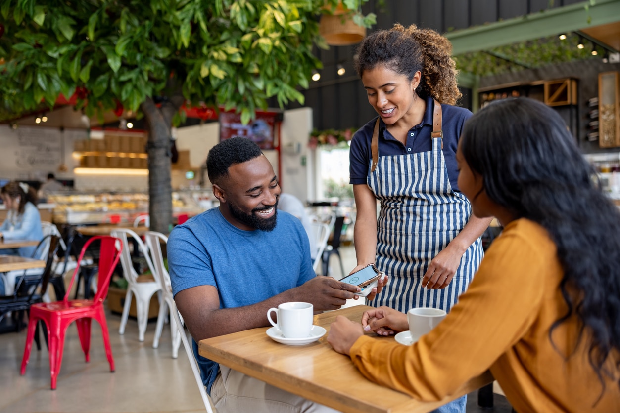 Man on a date making a mobile payment to the waitress at a coffee shop