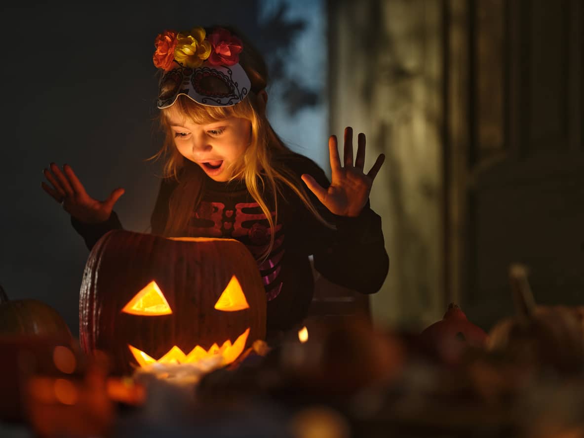 Surprised little girl looking inside of Jack O' Lantern on Halloween