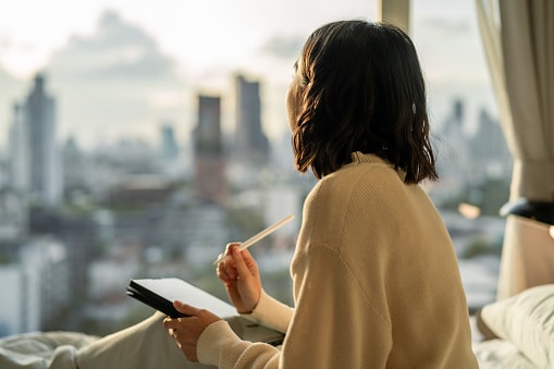 Woman looking out the window, writing her new year's resolution on her iPad
