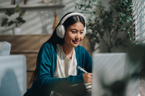 Woman wearing headphones, looking at her laptop.