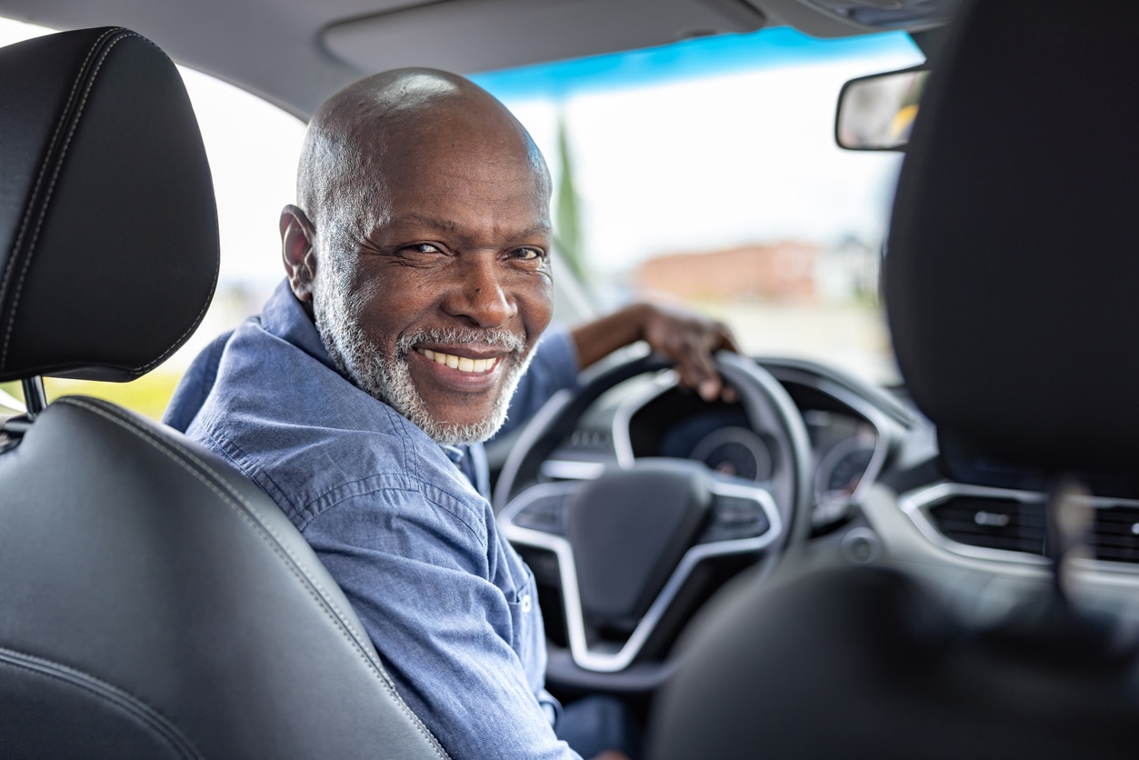 Senior man in a car looking back at the passenger seat and smiling.