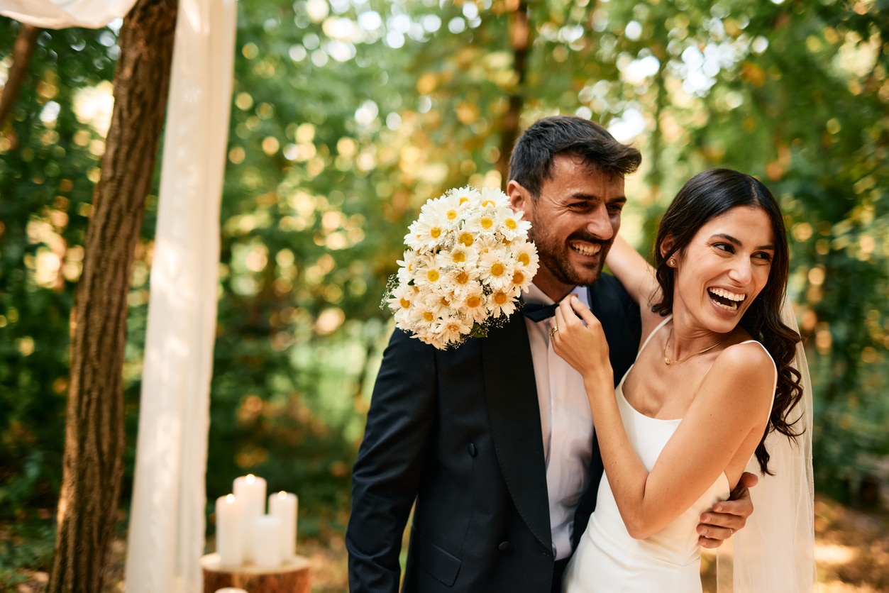 Happy newlyweds laughing and hugging in the woods during their wedding ceremony