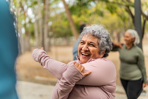 Senior woman stretching and talking friend at public park.